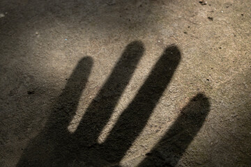 The shadow of a human hand on a rough ground texture, created by strong light. An abstract concept of loneliness, fear, or reaching.