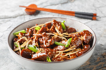Stir fried beef ginger with lightly sweet sauce, green onion and sesame closeup in the bowl on the table. Horizontal