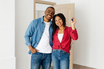 Happy African American couple celebrating home ownership, woman holding house keys, cheerful black spouses smiling warmly while standing together near the doorway, copy space