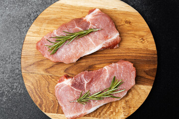 Fresh pork chops with rosemary on a wooden cutting board in a kitchen