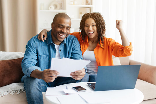 Excited young black spouses with papers celebrating good news at home, happy african american couple reading documents and enjoying success, emotionally reacting to financial profit - Powered by Adobe