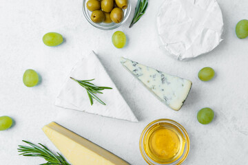 Cheese platter with olives, grapes, and rosemary arranged on a light background