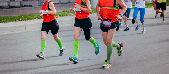 two women and man running marathon in city, green compression socks on his feet