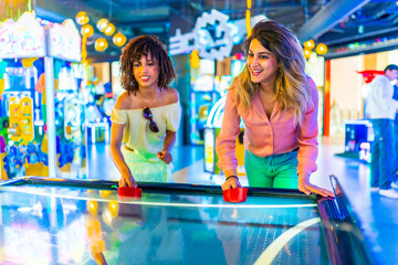 Two happy women playing air hockey in an amusement arcade