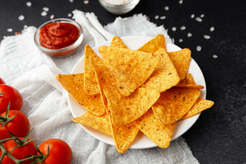 Plate of nachos with tomato sauce and tomatoes on white cloth on black surface