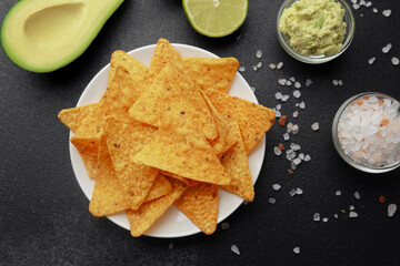 Nacho chips with avocado, lime, salt and guacamole on black background