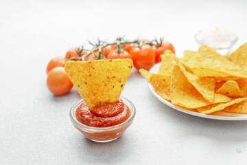 Closeup of nacho chip dipped in salsa with plate of chips and tomatoes