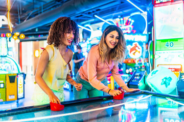 Two female friends playing air hockey in a colorful arcade