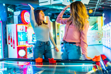 Two female friends giving high five while playing air hockey in arcade