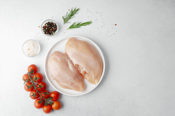Raw chicken breast on white plate with salt, pepper, rosemary and cherry tomatoes