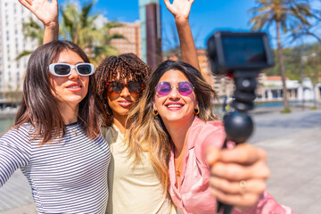 Happy friends taking selfie with action camera waving at city in summer