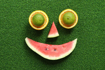 Fruit face. Orange and lime halves, watermelon slice on green grass background, top view. Fruit...