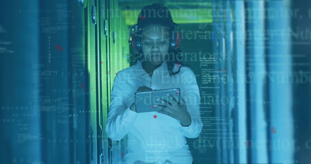 Female IT technician with red headset checking server status in data center, with tablet