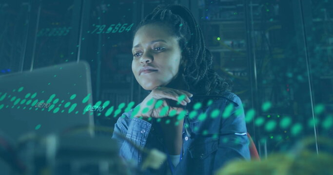 Monitoring woman wearing denim shirt analyzing system on laptop in server room, with blinking racks