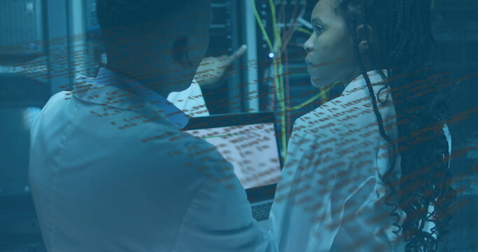 Pointing techs in lab coats examining server racks and Ethernet cables in server room, with laptop