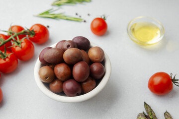 Red kalamata olives in bowl with tomatoes herbs and oil on white background