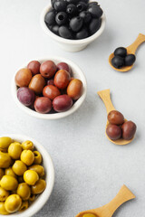 Variety of olives in bowls with wooden spoons on gray background, green olives, black and kalamata olives.