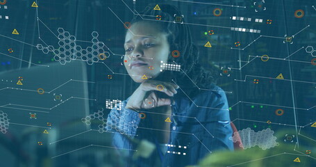 Gazing woman wearing denim shirt examining glowing monitor and data graphics before server racks