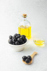 Black olives in bowl with bottle of olive oil on light background