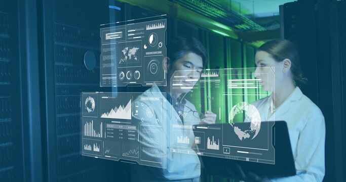 Two IT experts analyzing floating data holograms in server room corridor, with laptop and stylus
