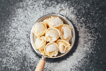 Flour dusted cappelletti pasta in strainer on dark kitchen background