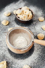 Flour dusted cappelletti pasta in strainer on dark kitchen background