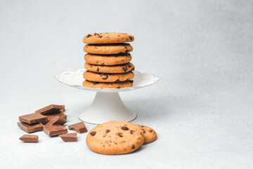 Delicious chocolate chip cookies stacked on a cake stand beside chocolate pieces