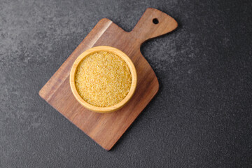 Cracked wheat groats in wooden bowl on black background. Healthy raw cereal grains.