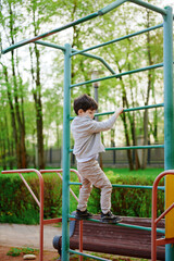 Obraz premium child climbing jungle gym outdoors captures playful energy in lush park setting. young boy enjoying adventure on playground equipment, balancing skillfully in casual attire.