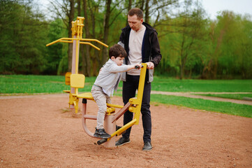 father and son enjoying outdoor exercise equipment in park. bonding moment shows family fitness,...