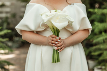 The bride in a white wedding dress holds a bouquet of white flowers - callas.. Wedding. Bride and...