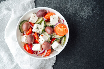 Greek salad with feta cheese olives cucumbers tomatoes and onions in white bowl on dark background with napkin