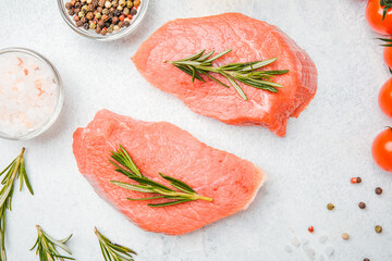 Top view of veal steaks with spices and herbs on white background including close-up of oil and...