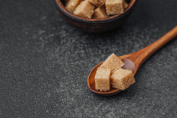 Brown sugar cubes arranged in a wooden spoon on a dark background