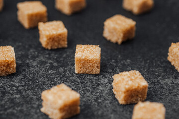 Brown sugar cubes scattered on a dark surface at a kitchen setting