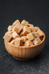 Brown sugar cubes in a wooden bowl on a dark surface for cooking