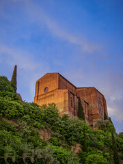 Basilica Cateriniana di San Domenico church rises above Siena, its imposing Gothic architecture framed from a low vantage point against the Tuscan sky. Travel in Italy.