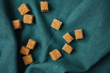 Brown sugar cubes scattered on a textured teal fabric background
