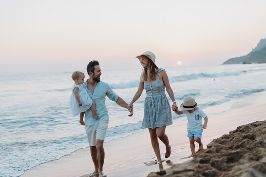 Fototapeta Young family walking on sandy shore during summer beach holiday.