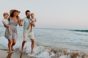 Young family walking on sandy shore during summer beach holiday.