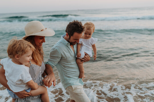 A family with two toddler children walking on beach on summer holiday at sunset.