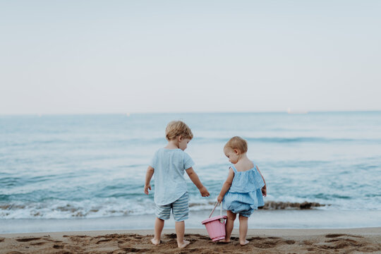 Two toddler children playing on sand beach on summer holiday.