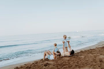 Gordijnen Parents lying in sand and having fun with kids on beach on summer holiday. © Halfpoint