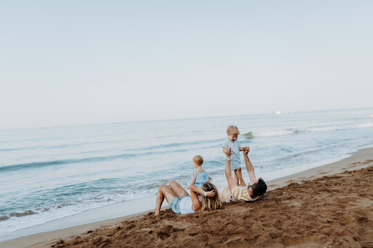 Parents lying in sand and having fun with kids on beach on summer holiday.