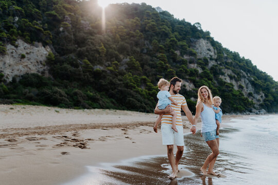 Fototapeta Young family walking on sandy shore during summer beach holiday.