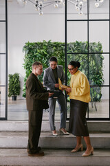 Vertical shot of two young adult women and man standing together in modern office discussing...