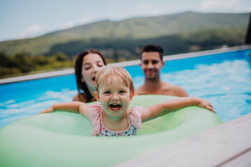 Fototapeta premium Young family with small daughter in swimming pool outdoors in backyard garden.