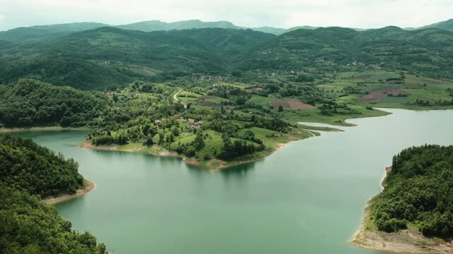 Panoramic view of winding shoreline of Rovni Lake with villages and hills in spring, Valjevo, Serbia. Horizontal 4k footage.