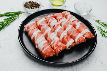 Bacon wrapped sausages on black plate with spices and rosemary