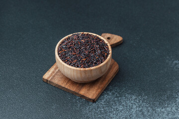Black rice in wooden bowl on cutting board over dark background